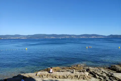 Vista desde punta Faxilda. El mar azul se extiende hasta la costa montañosa, con un kayak solitario y boyas amarillas.