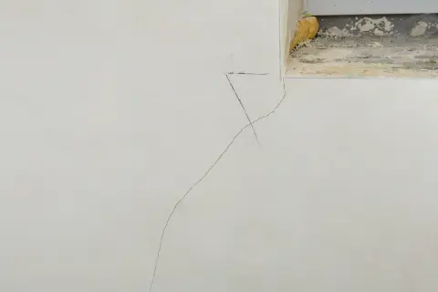 Grieta fina en pared de yeso, indicando la necesidad de reparar grietas por asentamiento. Se observa una marca de lápiz cerca de la grieta.