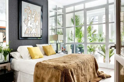 Dormitorio de matrimonio moderno con manta peluda y arte abstracto. Las ultimas tendencias en decoracion de dormitorios de matrimonio se reflejan en la luz natural y las plantas.