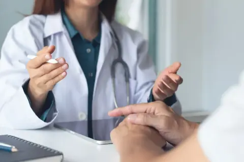 Lekarz w białym kitlu rozmawia z pacjentem, omawiając jego stan. Pytanie, czy rehabilitant może wystawić L4, jest kluczowe dla wielu osób.