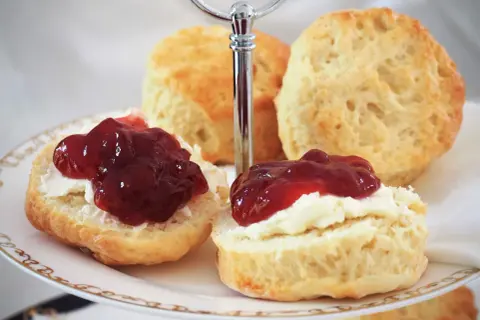 Zwei Scones mit Clotted Cream und Marmelade auf einer Etagere. Ein köstliches Rezept für Scones, das man unbedingt ausprobieren muss!