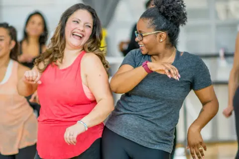 Zwei Frauen lachen und tanzen ausgelassen bei einem Zumba-Kurs. Ein toller Weg, um den **Zumba Kalorienverbrauch** zu steigern und Spaß zu haben!