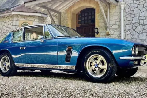Blå Jensen Interceptor parkerad framför ett stenhus.