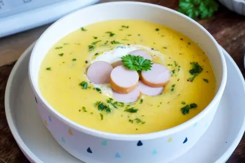 Cremige Kartoffelsuppe, zubereitet im Thermomix, garniert mit Würstchenscheiben, einem Klecks Sahne und Petersilie.