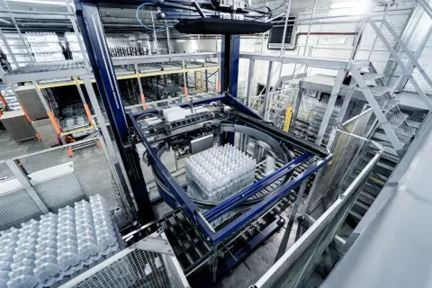 Automatyczne gniazdo produkcyjne pakuje butelki z wodą. Maszyna obraca paletę z napojami, przygotowując ją do dalszego transportu.