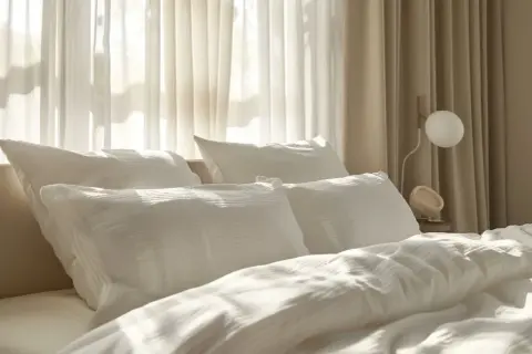 Gemütliches Bett mit weißen Kissen und Decken. Die sanften Falten der Bettwäsche lassen vermuten, dass sie aus einem Material wie Polyester ist, das überraschend warm halten kann.