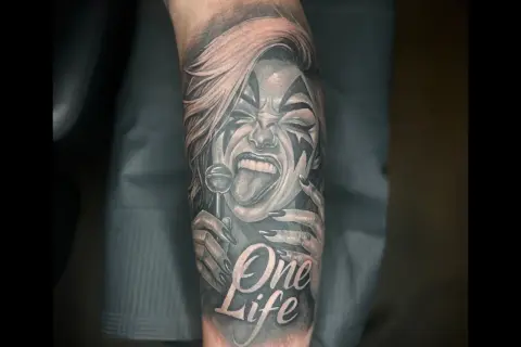 Ein detailreiches Tattoo mit einer Frau, die einen Lolli leckt, und der Aufschrift "One Life". Das Kunstwerk ist in Schwarz und Rot gehalten.