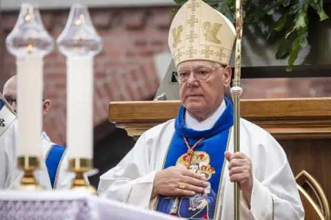 Kardynał w mitrze i szacie z pastorałem, trzyma rękę na piersi.