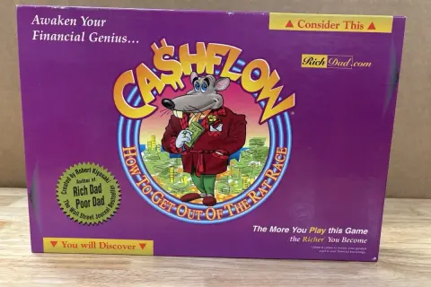 Das Cover des **Cashflow Spiels** zeigt eine Maus in einem Anzug, die Geld hält. Es ist ein Brettspiel, das finanzielle Bildung vermittelt.