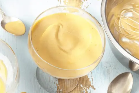 Cremiges Zabaione-Rezept in einem Glas, Löffel daneben. Ein Schneebesen ruht in einer Schüssel mit der köstlichen Masse.