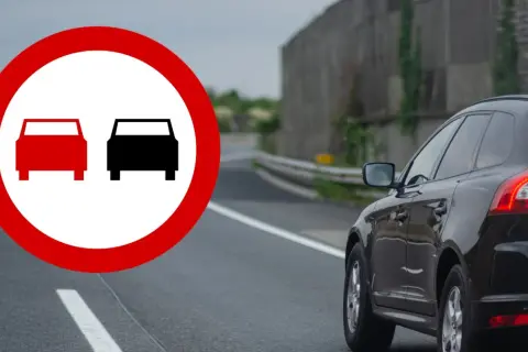 Znak zakazu wyprzedzania na drodze jednokierunkowej. Czarny SUV jedzie po drodze, gdzie wyprzedzanie jest zabronione.