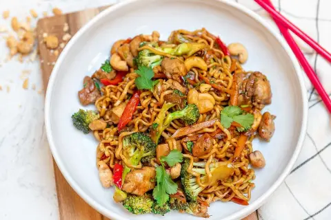 Enkel mat: en skål med nudlar med kyckling, broccoli, paprika och cashewnötter. Röd pinnmat ligger bredvid.