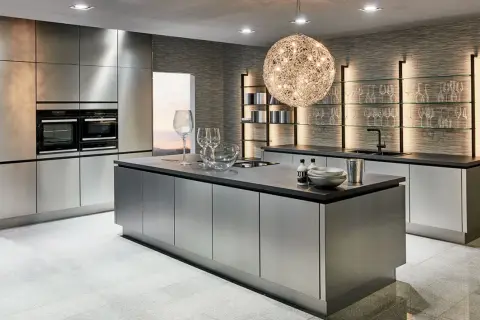 Une cuisine chic et moderne aux finitions métalliques, avec un îlot central, des fours intégrés et des étagères lumineuses.