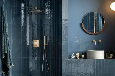 Élégante salle de bain bleu nuit avec douche à l'italienne carrelée, miroir rond en bois et vasque en béton.