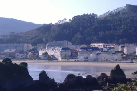 Vista de la playa vivero con edificios y colinas verdes al fondo.