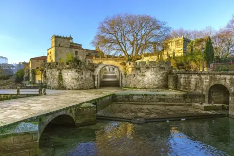 El pazo Vista Alegre, con su puente de piedra y río, se alza majestuoso bajo un cielo azul.