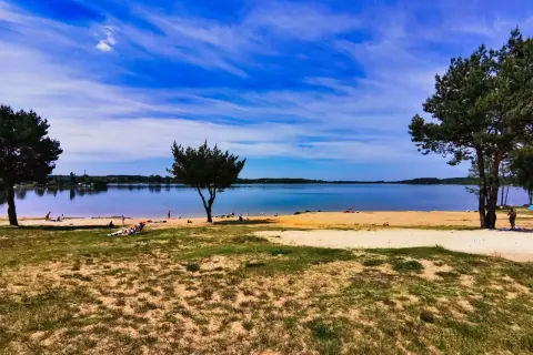 Słoneczny dzień nad jeziorem Pławniowice. Ludzie odpoczywają na piaszczystej plaży, ciesząc się błękitem nieba i spokojną wodą.