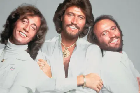 Trzej bracia z Bee Gees, Barry, Robin i Maurice Gibb, uśmiechają się do zdjęcia. Kto żyje? Barry i Robin.