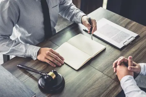 Avvocato e cliente discutono, con un martelletto da giudice e un quaderno aperto. Il ctu significato è fondamentale per la giustizia.