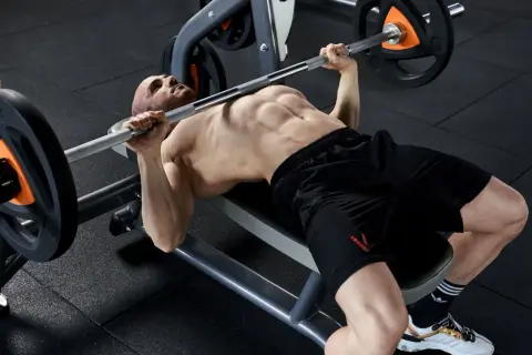 Uomo muscoloso esegue un allenamento powerlifting con bilanciere su panca piana in palestra.