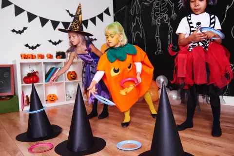 Niñas disfrazadas de bruja y calabaza juegan a lanzar aros en sombreros de bruja, parte de divertidos juegos de Halloween para niños.