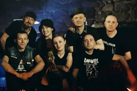 Grupa przyjaciół, zespół Leniwiec, pozuje do zdjęcia w mrocznym wnętrzu.