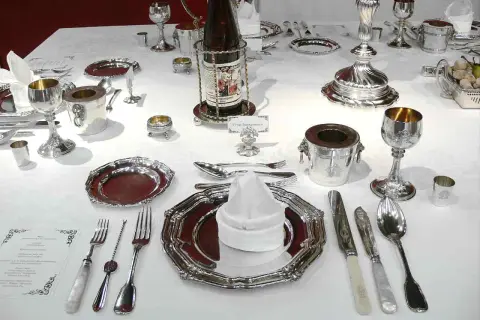 Une table dressée pour un service à l'anglaise, avec vaisselle en argent, verres, couverts et bouteille de vin.