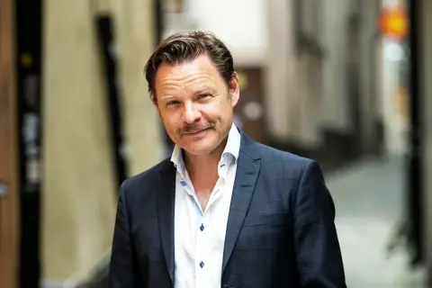 Kasper Sulocki, en man med mustasch, bär en mörkblå rutig kavaj och vit skjorta i en gränd.