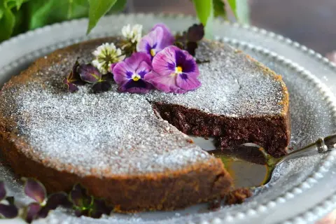 En saftig tårta med chokladpudding, pudrad med florsocker och dekorerad med violer och klöver. En bit är uppskuren.