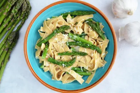 Makaron tagliatelle z zielonymi szparagami i startym parmezanem w niebieskiej misce.