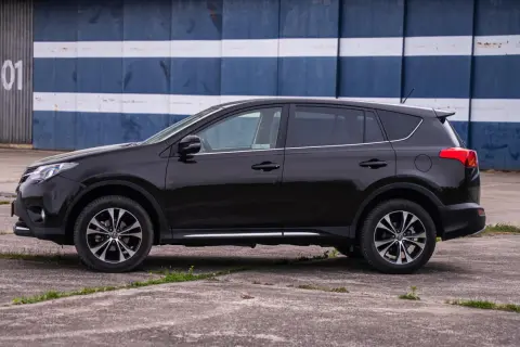 Czarny, używany Toyota RAV4 z salonu, zaparkowany przed budynkiem z niebiesko-białymi pasami.