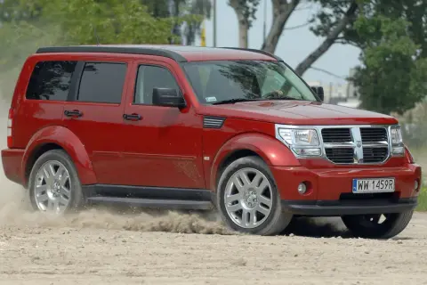 Czerwony Dodge Nitro z impetem wjeżdża na piaszczystą drogę, wzbijając tumany kurzu.