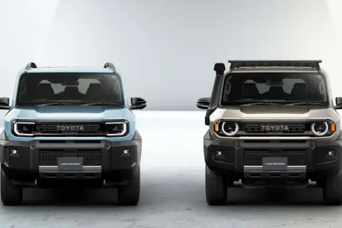 Dwa nowe modele Toyota Land Cruiser, jeden błękitny, drugi złoty, z charakterystycznym grillem i okrągłymi światłami.