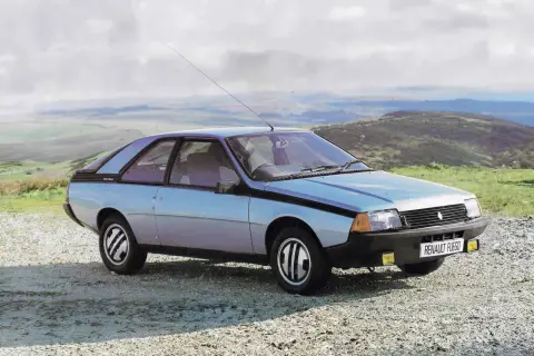 Jasnoniebieski Renault Fuego z lat 80. stoi na szutrowej drodze, z widokiem na pagórkowaty krajobraz i chmurne niebo.