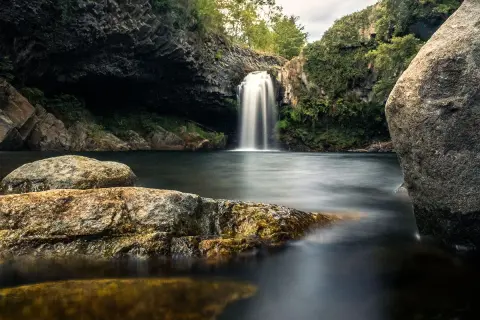 Magnifique cascade piscine naturelle en Ardèche, entourée de rochers et de végétation luxuriante. L'eau tombe en voile blanc dans le bassin sombre.