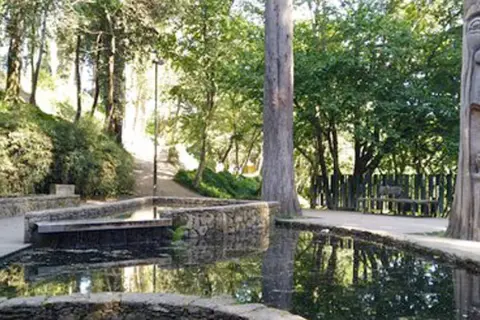 Escultura de madera en el parque de los sentidos, junto a estanques de agua y vegetación exuberante.