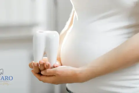 Mani di donna incinta tengono un dente bianco, simbolo della cura per la pulizia dei denti in gravidanza.