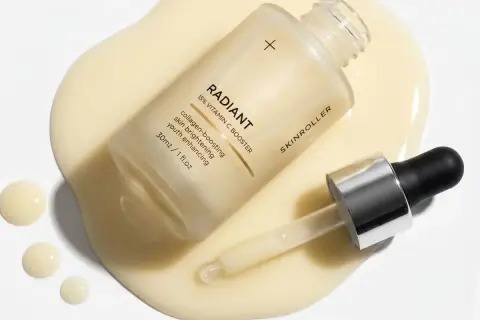 En flaska med "RADIANT 15% VITAMIN C BOOSTER" serum ligger på en gulaktig vätska. Pipetten har en droppe pha syra redo att appliceras.