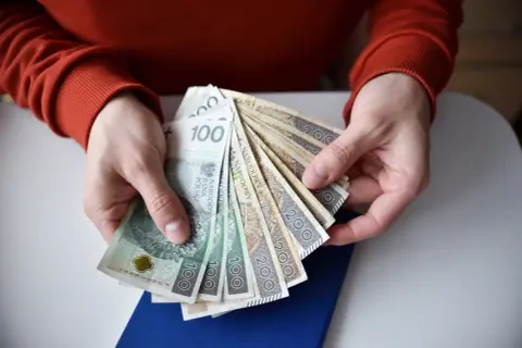 Ręce trzymają polskie banknoty 100 i 200 zł. Zastanawiasz się, ile wynosi renta po świadczeniu rehabilitacyjnym?