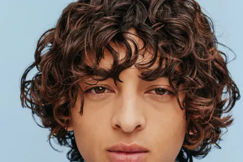 Gros plan sur le visage d'un homme aux cheveux bruns ondulés, type cheveux 2b homme, sur fond bleu clair.