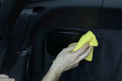 Hand reinigt mit gelbem Tuch den schwarzen Kunststoff im Auto.