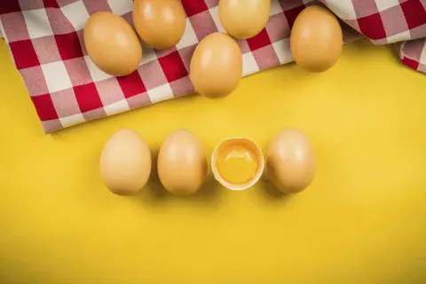 Uova su sfondo giallo, una rotta mostra il tuorlo. Quante uova si possono mangiare al giorno?