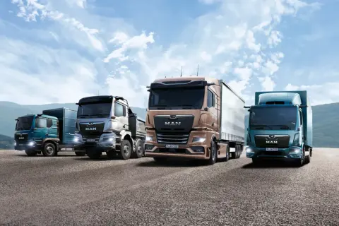 Quatre camions de la marque MAN, aux couleurs variées, roulent sur une route sous un ciel bleu nuageux.