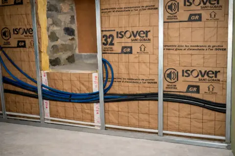 Pose rail placo pour isolation acoustique Isover. Tuyaux bleus et noirs passent derrière.