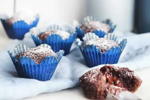 Kladdkakemuffins recept: Mjuka chokladmuffins i blåa pappersformar, pudrade med florsocker. En är uppskuren och visar en härligt kladdig insida.