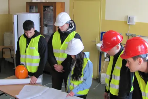 Uczniowie technikum w kamizelkach odblaskowych i kaskach analizują plany, przygotowując się do zdobycia uprawnień budowlanych.