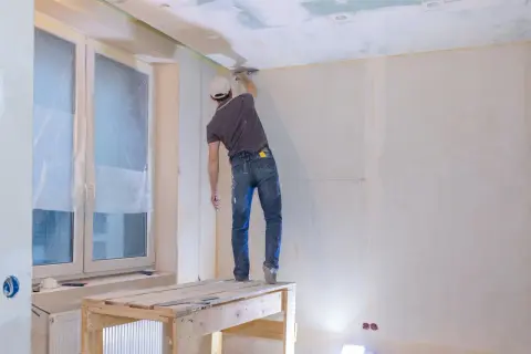 Pracownik na rusztowaniu szpachluje sufit. Poznaj atrakcyjną szpachlowanie cena za usługę.
