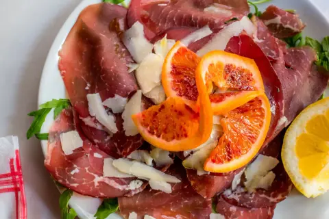 Bresaola co to? Delikatne plastry wędzonego mięsa wołowego, posypane parmezanem, z dodatkiem krwistych pomarańczy i cytryny.