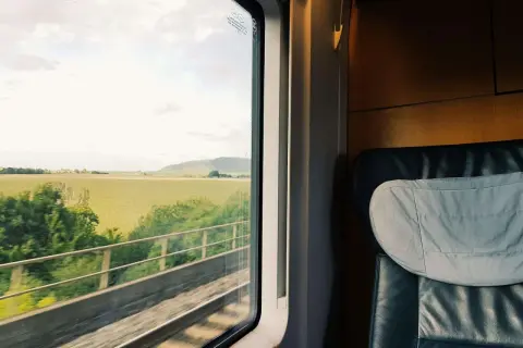 Blick aus dem Zugfenster auf grüne Felder während der zugreise nach wien. Ein bequemer Sitz im Vordergrund.
