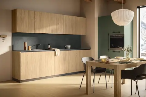Cucina moderna con mobili in legno chiaro e pensili alti. La zona pranzo è apparecchiata, con una vista panoramica innevata dalla finestra. L'altezza dei mobili cucina è ben studiata per funzionalità ed estetica.